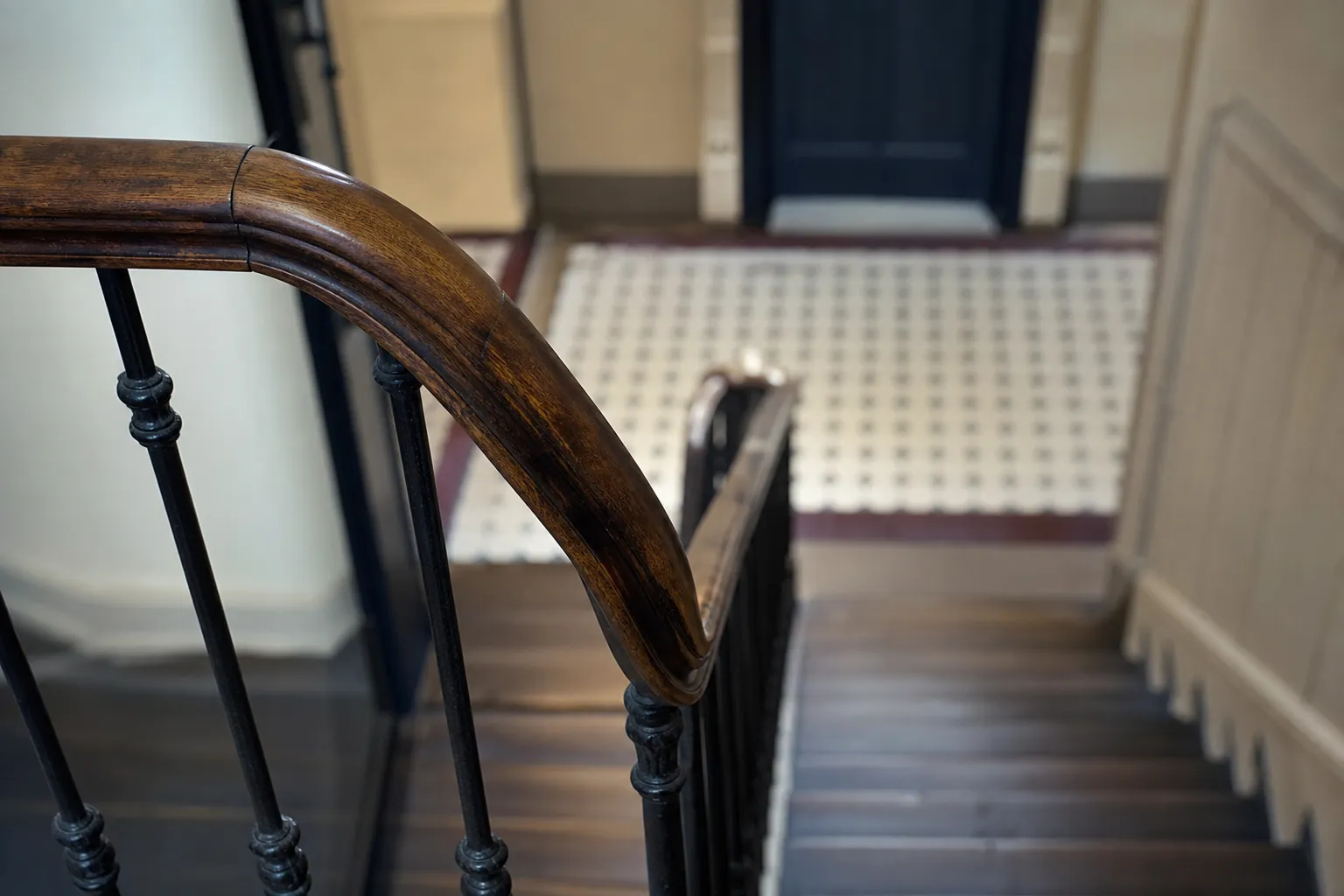 Cage d’escalier ancienne avec rampe en bois et carrelage au sol